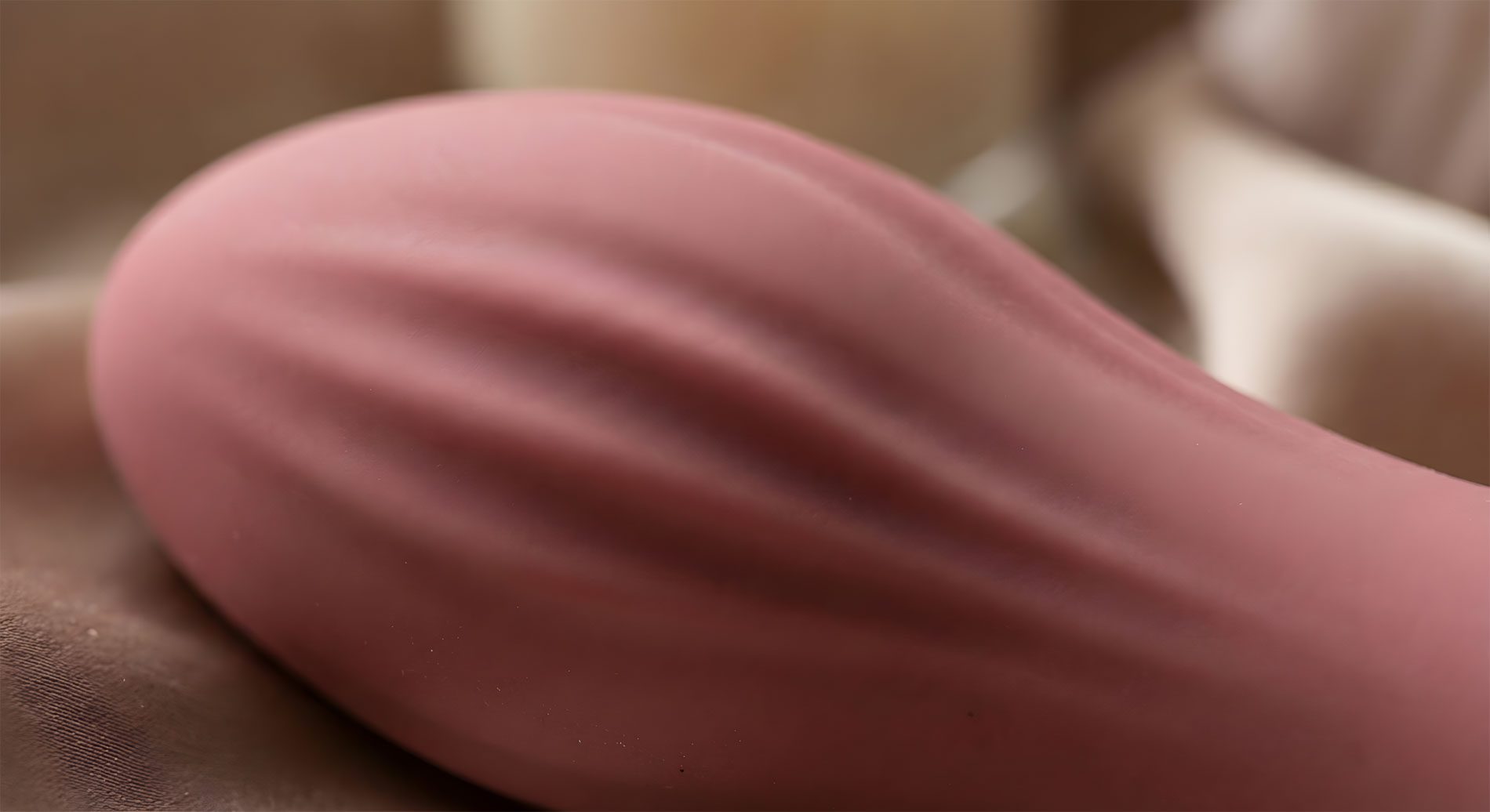 Primo piano macro di un accessorio in silicone vellutato color cipria con texture a coste, adagiato su un tessuto di seta raffinato.