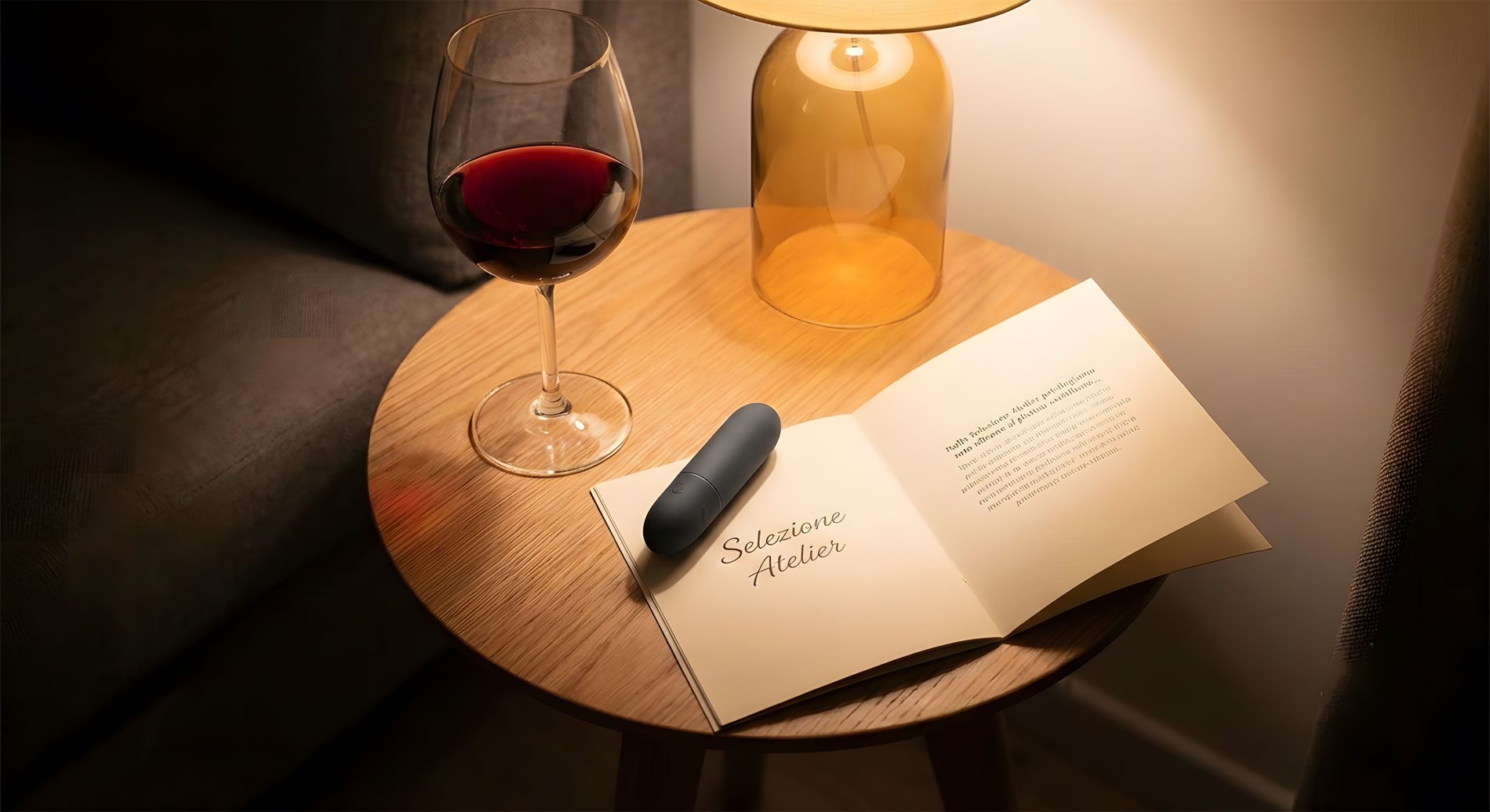 Un calice di vino rosso e un accessorio discreto appoggiati su un libro aperto con la scritta Selezione Atelier su un tavolino in legno, atmosfera calda.