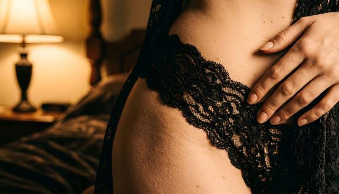 Dettaglio macro di pizzo nero su pelle nuda con mano femminile in luce ambrata calda, lingerie come primo strato sensoriale del rituale —Eros Atelier